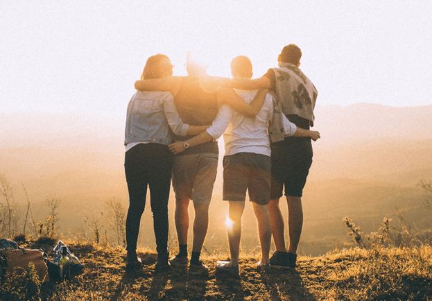 A group of friends with arms around each other watching a sunset